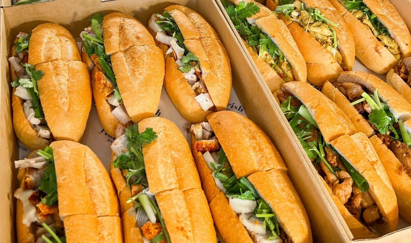 Rows of crusty bánh mì rolls filled with roast pork, chicken, coriander and spring onion