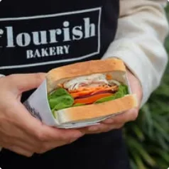 A Flourish team member holding a bánh mì in a paper bag