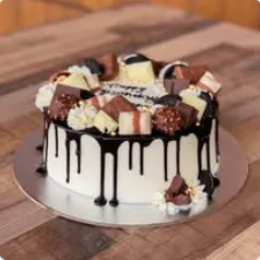 A birthday cake with chocolate drip, topped with chocolates and treats