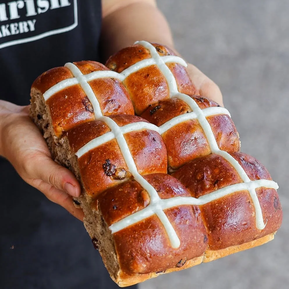 A tray of glazed hot cross buns held in two hands
