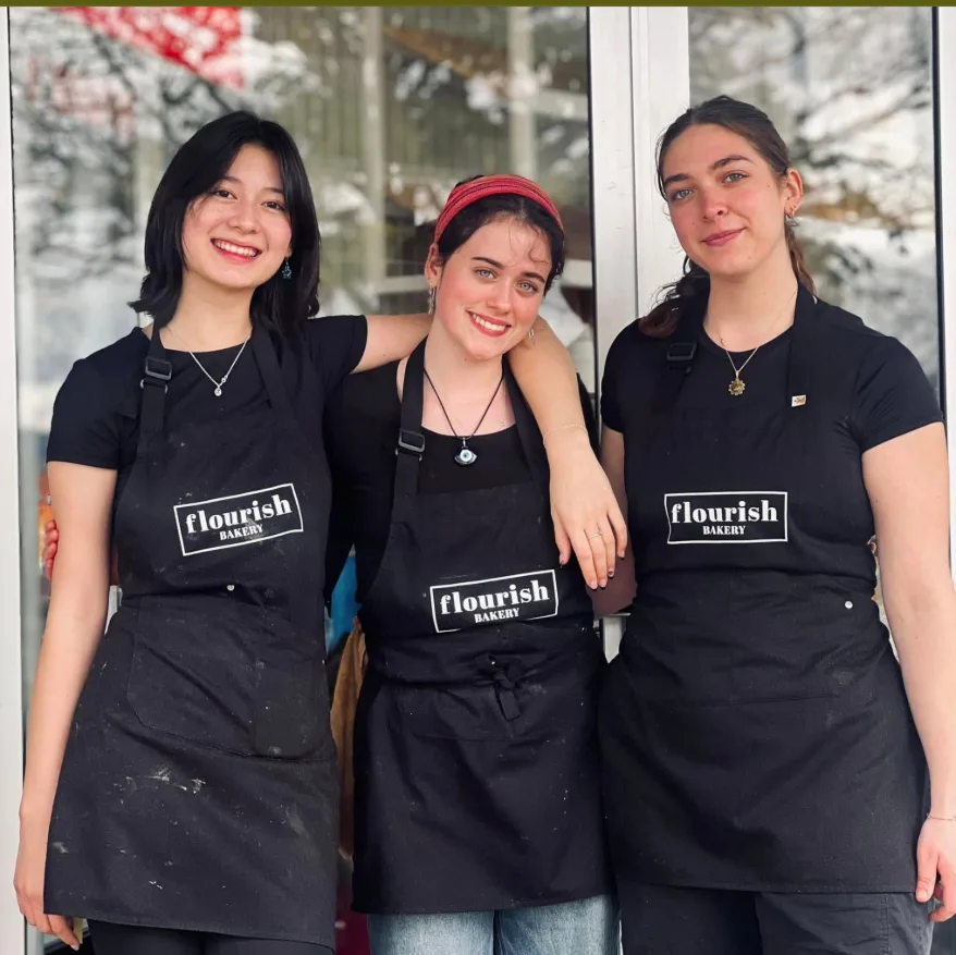 Three smiling team members in Flourish Bakery aprons outside the shop